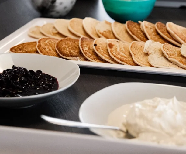 Stol s tanjurima palačinki, muffina, šlaga i preljevom od borovnica.