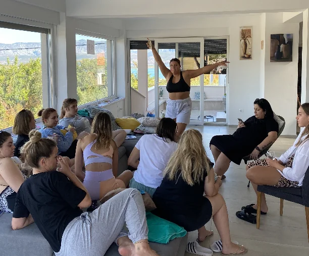 Žene okupljene u dnevnoj sobi moderne kuće dok Pamela stoji i govori.