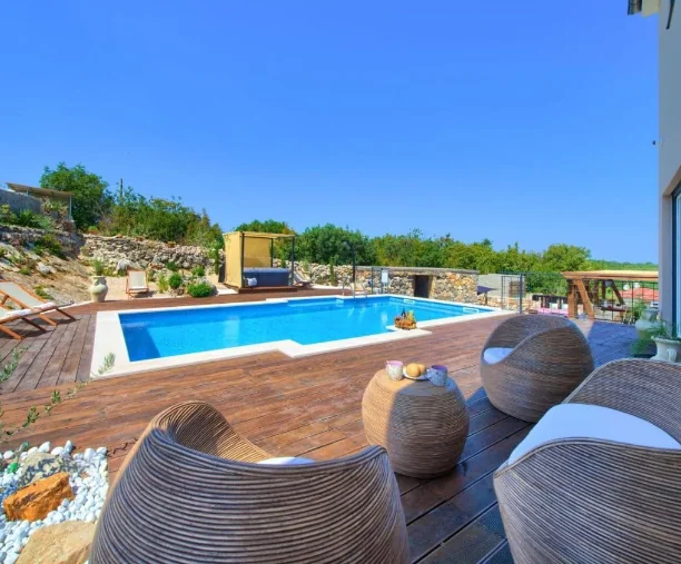 Moderno uređena terasa s udobnim sjedećim namještajem i bazenom okruženim zelenilom