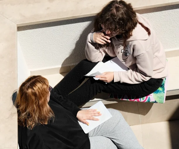 Dvije žene sjede na terasi u razgovoru, držeći papire u rukama